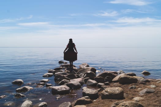 Silhouette of a woman standing on stones at the beach. beautiful summer landscape with horizon line. sea and sky