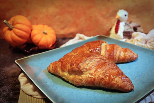 Two croissants on plate with a thanksgiving background.
