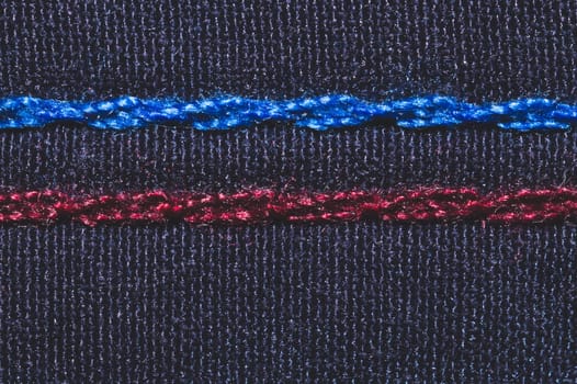 Blue and red seam on black fabric. stitches on textile material close up