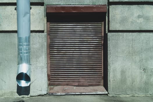 Corrugated iron blind on a concrete wall. drain pipe. metal curtain. closed window