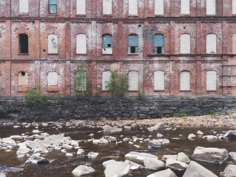 Abandoned factory on the water edge. old building on the rocky river. brown brick wall. water stream