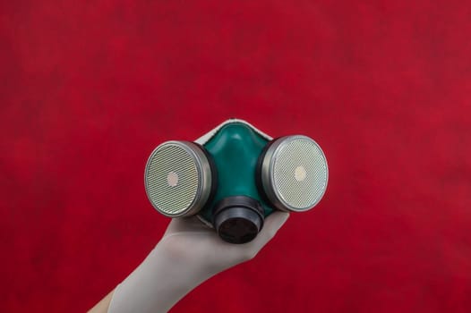 Respirator with replaceable filters. protection against respiratory threats. hand in a surgical glove holds protective mask on a red background
