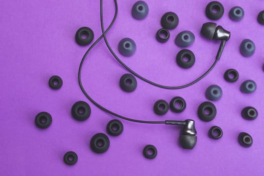 Earphones between of ear cushions on purple background. in-ear headphones and lot of embouchures. audio equipment