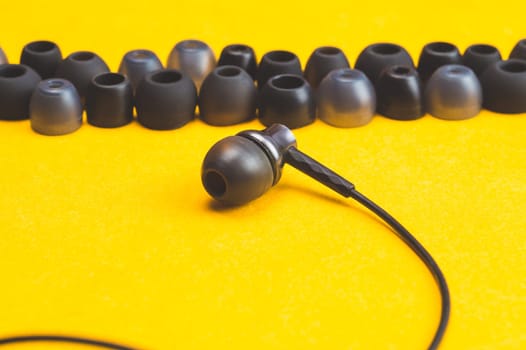 Earphones between of ear cushions on yellow background. in-ear headphones with many embouchures. modern style. audio equipment
