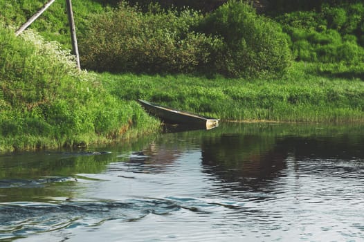 Old wooden boat near the riverside. overgrown shore. water surface
