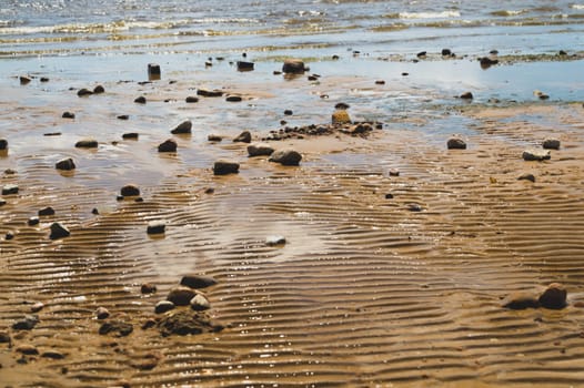 Stones on wavy wet sand. pebbles on the seashore close up. abstract background