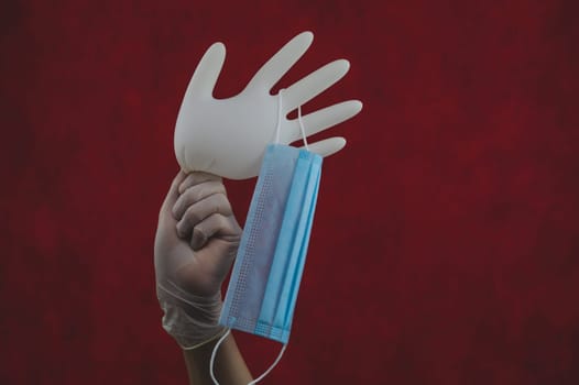 Medical mask hanging on inflated glove. hand holds white surgical glove with protective mask. red background