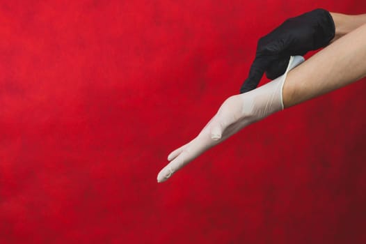 Hand in the black glove puts the white glove on the other. person puts on protective gloves on a red background