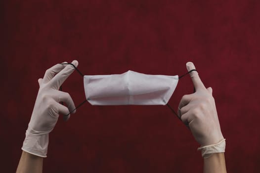 Hands in white gloves stretch a protective mask on a red background. preventive measures against respiratory illness and virus. hands in white surgical gloves holds mask for protection