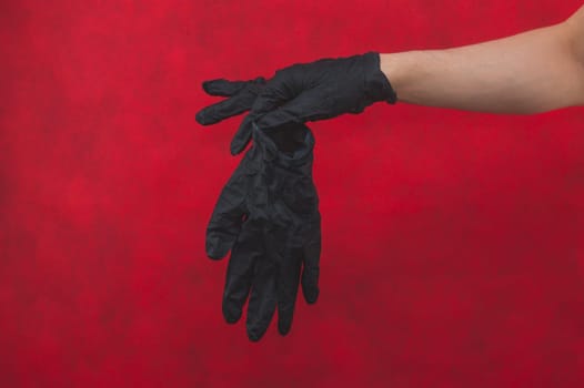 Hands in black medical gloves. person puts on surgical gloves on a red background