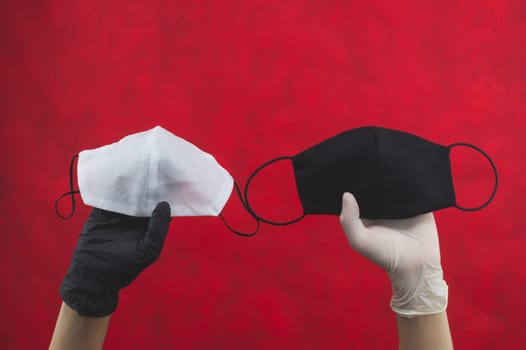 White protective mask in hand with black glove. black protective mask in hand with white glove. hands holds masks for protection. preventive measures against respiratory illness and virus