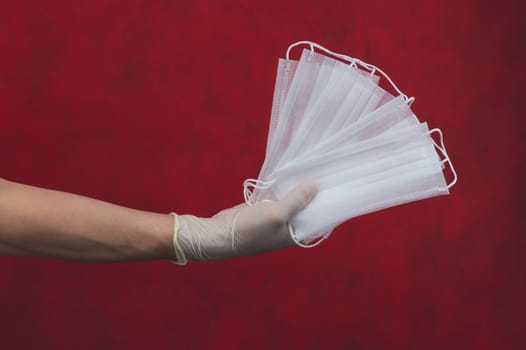 White medical masks in hand on a red background. preventive measures against respiratory illness and virus. hand in white surgical glove holds disposable masks for protection. copy space