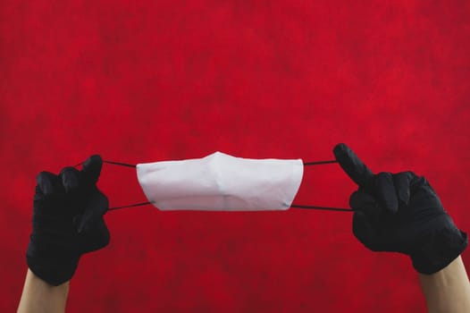 Hands in black gloves stretch a protective mask on a red background. preventive measures against respiratory illness and virus. hands in gloves holds mask for protection