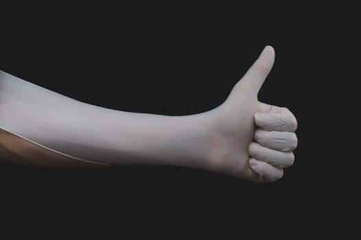 Hand in white medical glove shows thumbs up on a black background