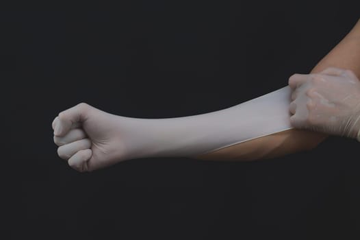 Hands in white medical gloves. person puts on surgical gloves on a black background. hand is clenched into a fist