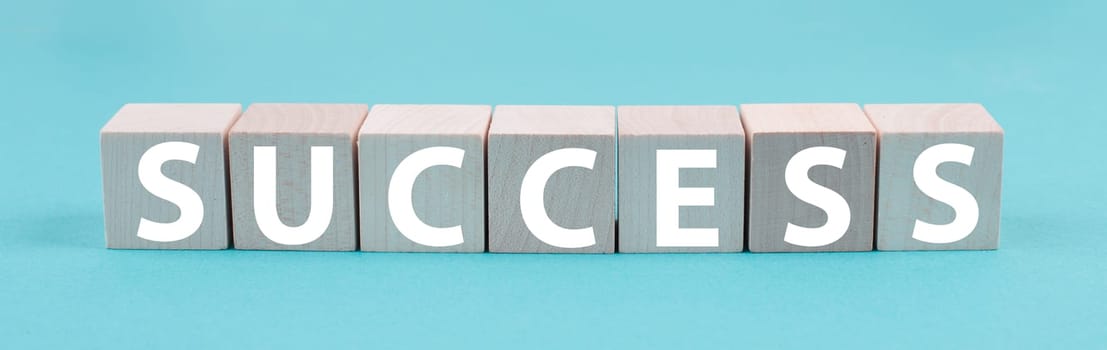 The word success is standing in white color on wooden cubes, blue background