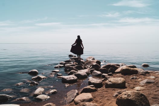 Silhouette of a woman standing on stones at the beach. beautiful summer landscape with horizon line. sea and sky
