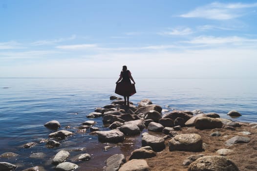 Silhouette of a woman standing on stones at the beach. beautiful summer landscape with horizon line. sea and sky