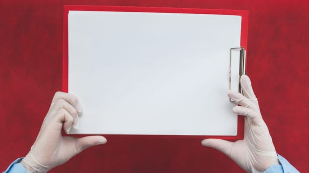 Hands in protective gloves holding white blank paper sheet on red background. template mock up. surface of leaflet. copy space