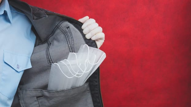 Man shows the protective masks in the pocket of jeans jacket. blue shirt. copy space. red background