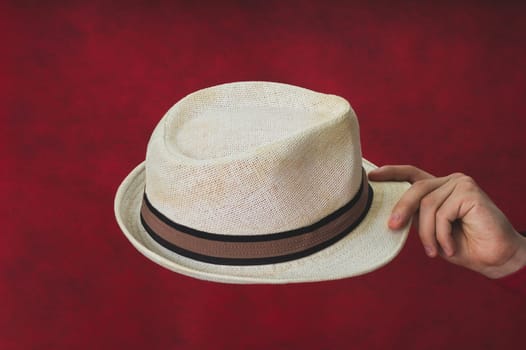 Hat in male hand on the red background. white fedora close up