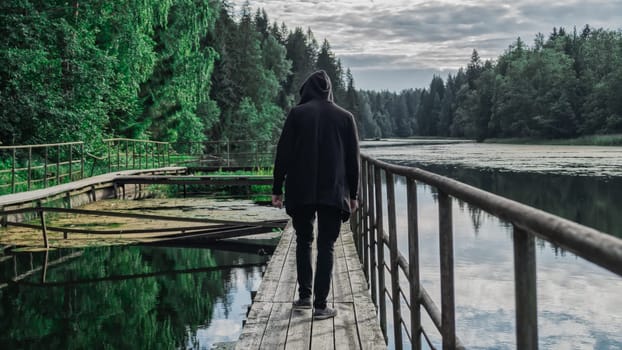 Man in the hood walks along the pier. back view