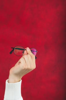 Hand holds eyeglasses on the red background