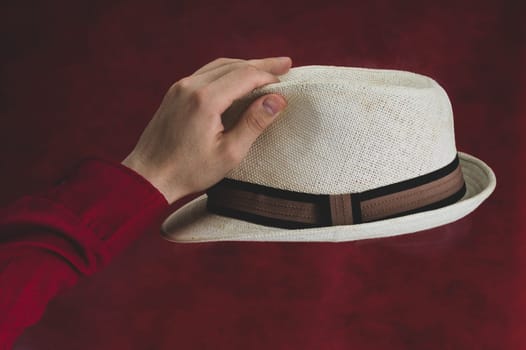 Hat in male hand on the red background. white fedora close up