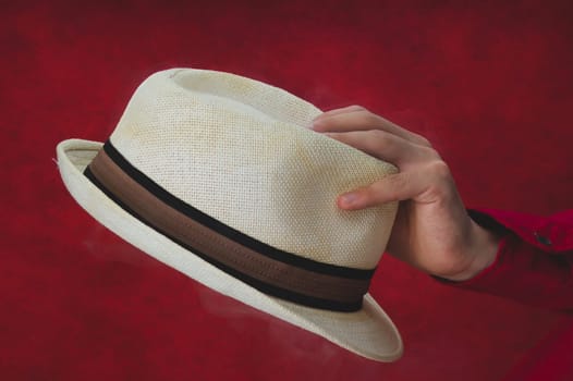 Hat in male hand on the red background. white fedora close up
