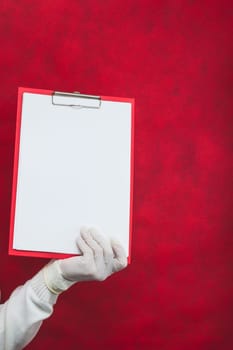 Hand in surgical glove holding white blank paper sheet on red background. template mock up. surface of leaflet. copy space