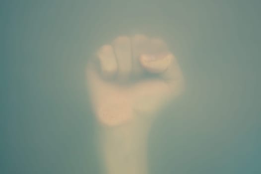 Fist behind frosted glass. silhouette of a raised up hand in the mist