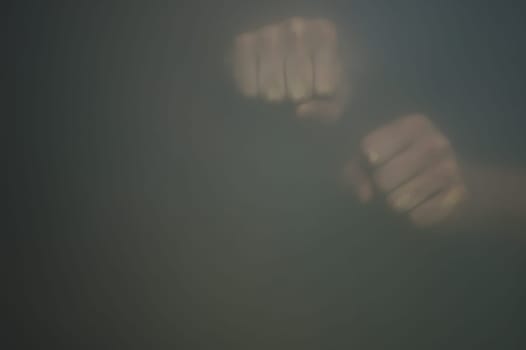 Fists behind frosted glass. silhouette of a clenched hands in the mist