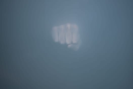 Fist behind frosted glass. silhouette of a clenched hand in the mist