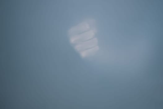 Fist behind frosted glass. silhouette of a clenched hand in the mist
