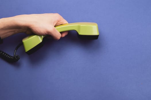 Hand holds classic telephone receiver. vintage green telephone handset on blue background. old communication technology. copy space