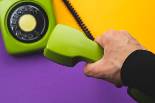 Hand holds classic telephone receiver. vintage green phone with handset on color background. old communication technology. copy space