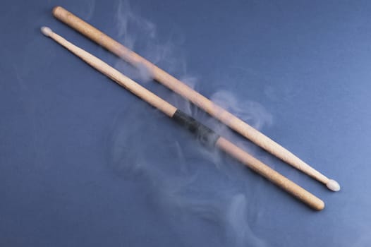 A pair of wooden drumsticks in the smoke on color background. copy space