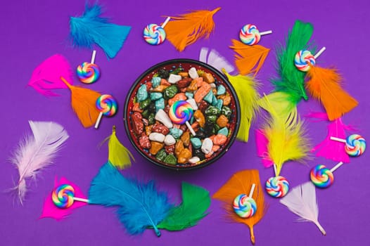 Candy pebbles in a bowl and lollipops. spiral candies and sweets in the form of colored stones. colorful feathers. festive background