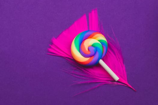 Lollipop lies on a feather. spiral candy on a colored background. festive decoration. copy space