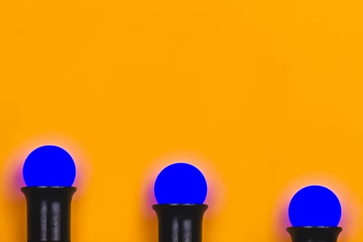 Blue light bulbs in lamp holders on a yellow background. colored bulbs with copy space