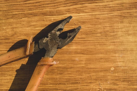 Pliers with orange handles on wooden background. work tool