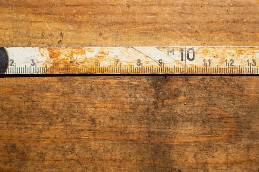 Old rusty ruler with black numbers on a working wooden table. vintage measuring tape. industrial background. carpentry workbench with copy space