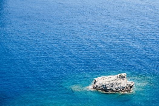 closeup top view of lonely rock surrounded by azure blue sea