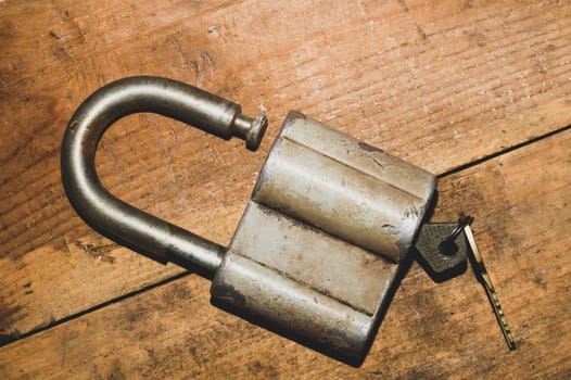 Old rusty lock with a key on a wooden table. Vintage padlock and key on wood background