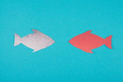 One red fish is swimming against the stream, opposite direction of the other fishes, being different