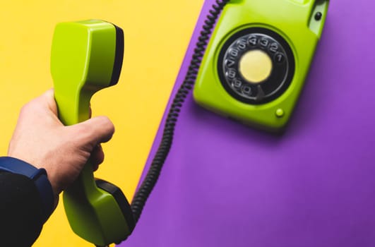 Hand holds classic telephone receiver. vintage green phone with handset on color background. old communication technology. copy space