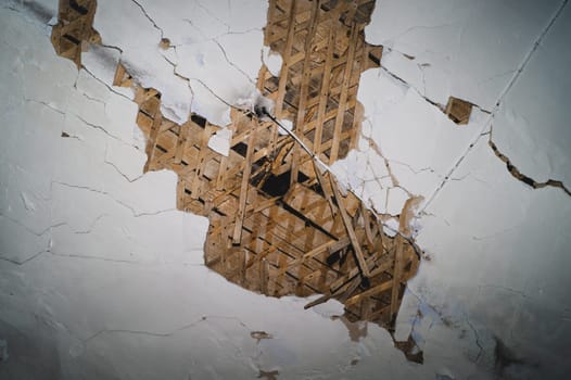 Dilapidated ceiling of an old house. damaged wall with a hole with timber frame. abstract background of ruined surface
