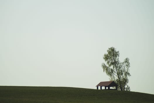 Lonely gazebo on the hill. summerhouse under tree standing alone in the field. solitude concept. shelter in the meadow