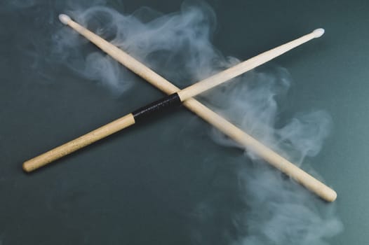 A pair of wooden drumsticks in the smoke on color background. copy space
