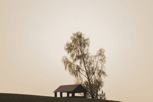 Lonely gazebo on the hill. summerhouse under tree standing alone in the field. solitude concept. shelter in the meadow